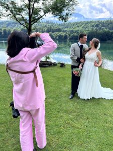 Hochzeitsfotografin bei der Arbeit am See – Brautpaar in traditionellem Outfit am Ufer, umgeben von grüner Natur