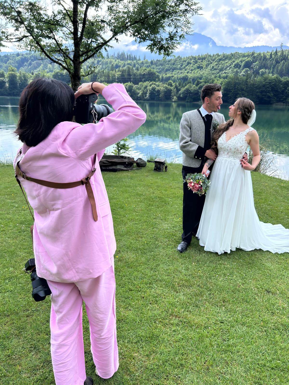 Hochzeitsfotografin bei der Arbeit am See – Brautpaar in traditionellem Outfit am Ufer, umgeben von grüner Natur