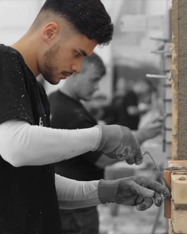 Ein junger Mann beim präzisen Mauern mit Kelle und Ziegel – Fokus auf Handwerk und Konzentration