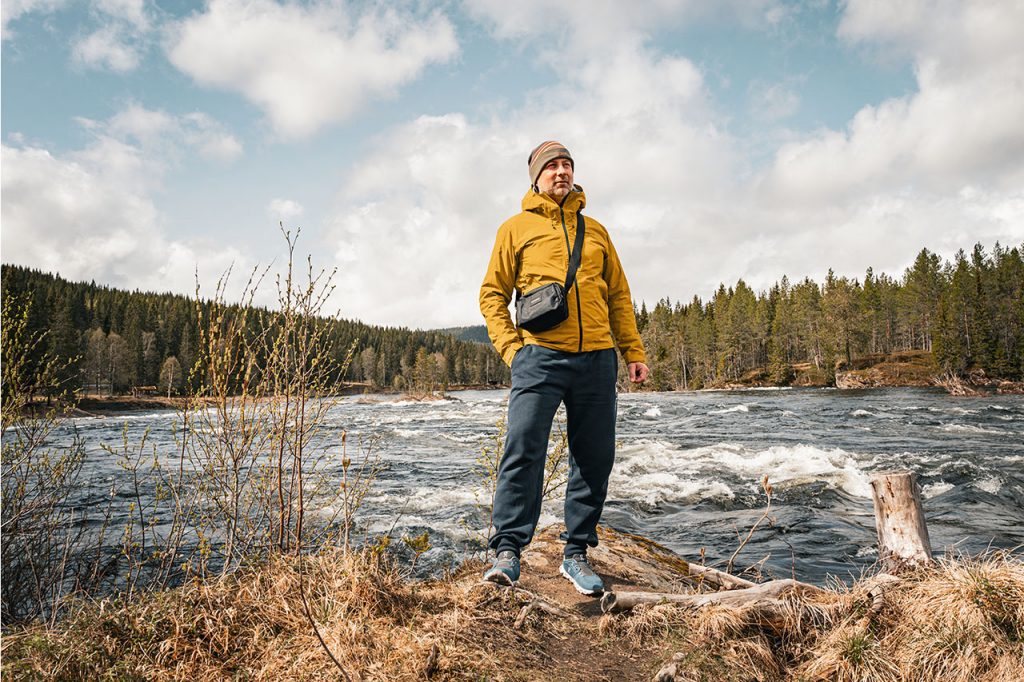 Mann steht in Outdoor-Bekleidung an einem wilden Fluss in der Natur