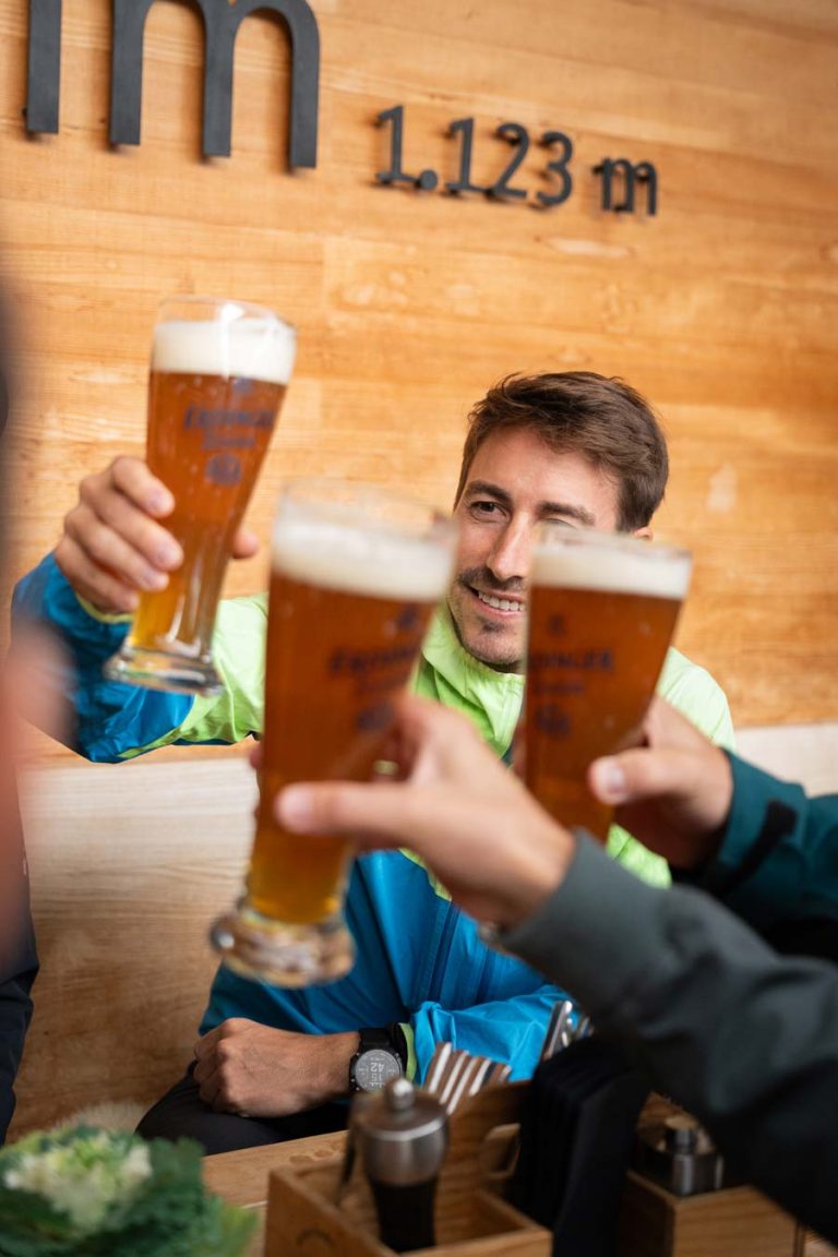 Gäste stoßen mit frisch gezapftem Bier auf der Umbrüggler Alm in Tirol an – geselliges Beisammensein auf 1.123 Metern Höhe.