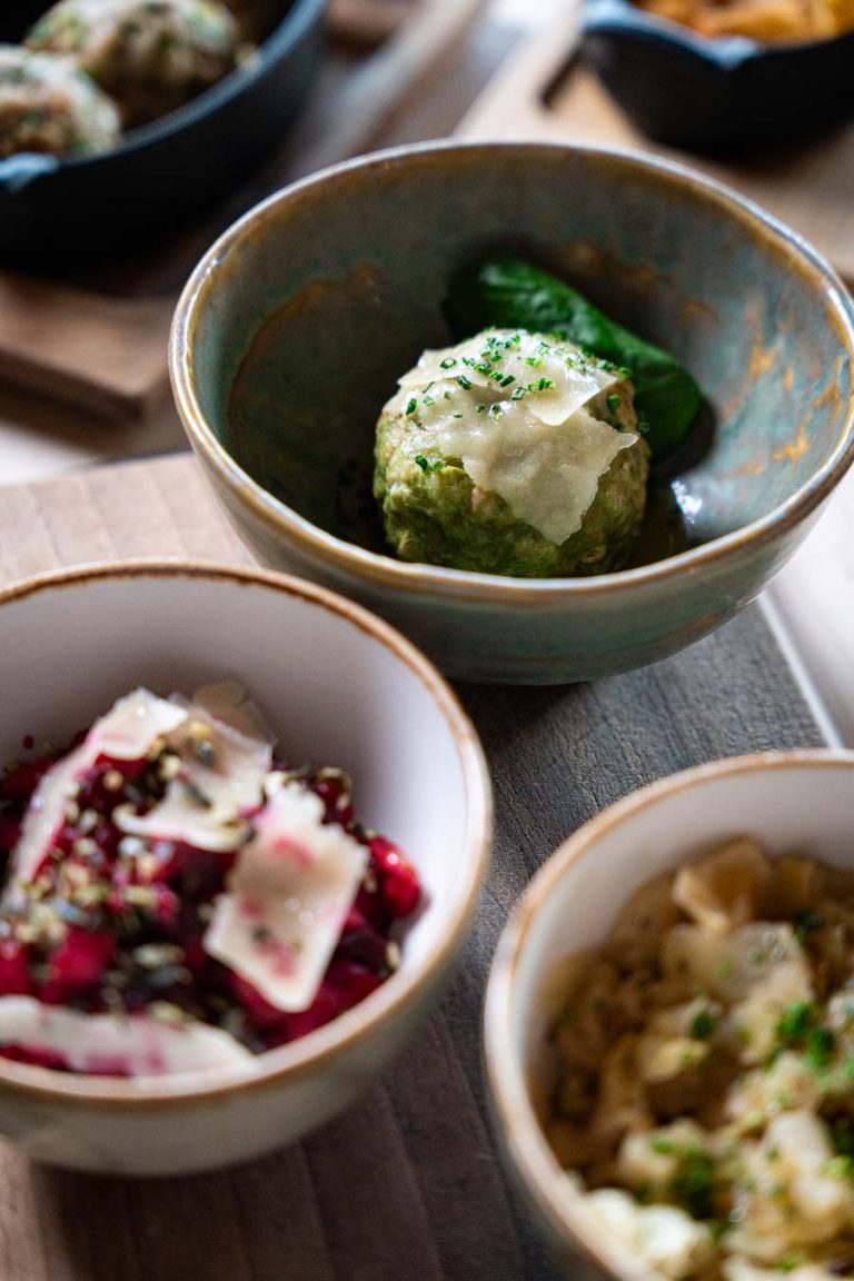 „Tiroler Spinatknödel mit Parmesan, serviert in rustikaler Keramikschale auf der Umbrüggler Alm in Innsbruck.