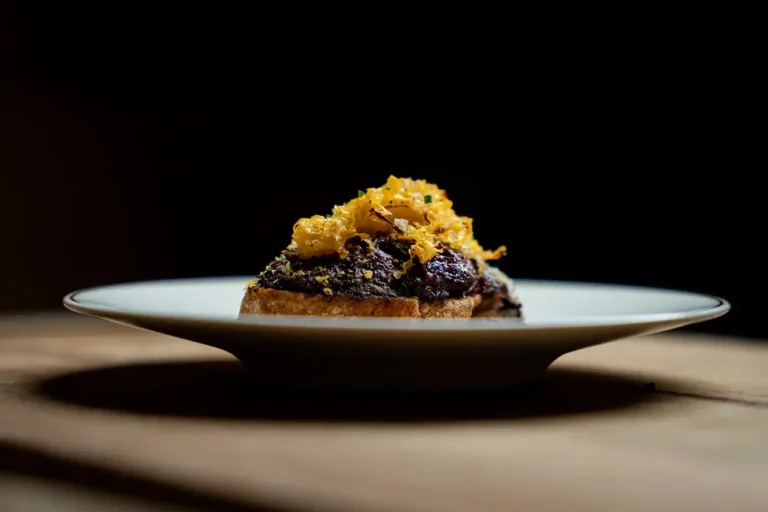 Fine Dining Vorspeise auf geröstetem Brot mit dunkler Creme und knusprigem Topping auf weißem Teller
