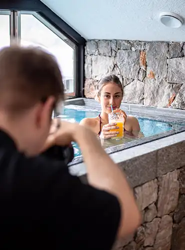 Frau entspannt im Indoor Whirlpool mit Orangensaft während Fotograf im Vordergrund ein Spa Shooting umsetzt