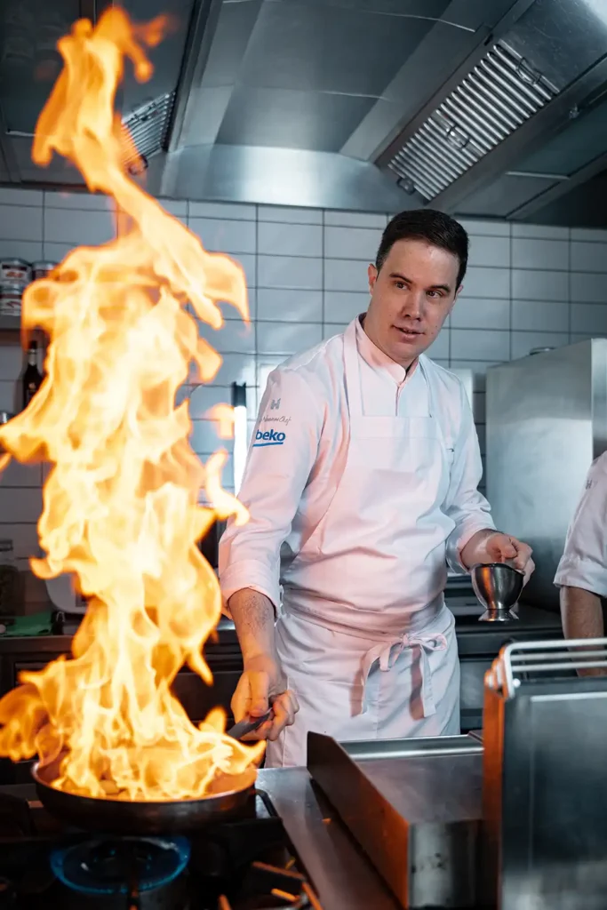 Koch flambiert Gericht in Restaurantküche mit hoher Flamme in der Pfanne